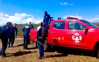 Un grupo de bomberos y una camioneta de color rojo, del cuerpo oficial de bomberos, preparandose con su equipo de buceo para realizar un inmersión en un embalse